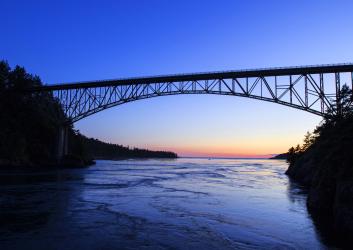Photo of a sunset over water with a towering bridge going over calm water.