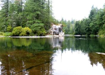 A wide view of placid, water reflecting green trees and open rock faces at Flaming Geyser State Park. 