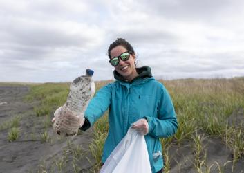 Woman with sunglasses and teal jacket holding a trash bag and litter.